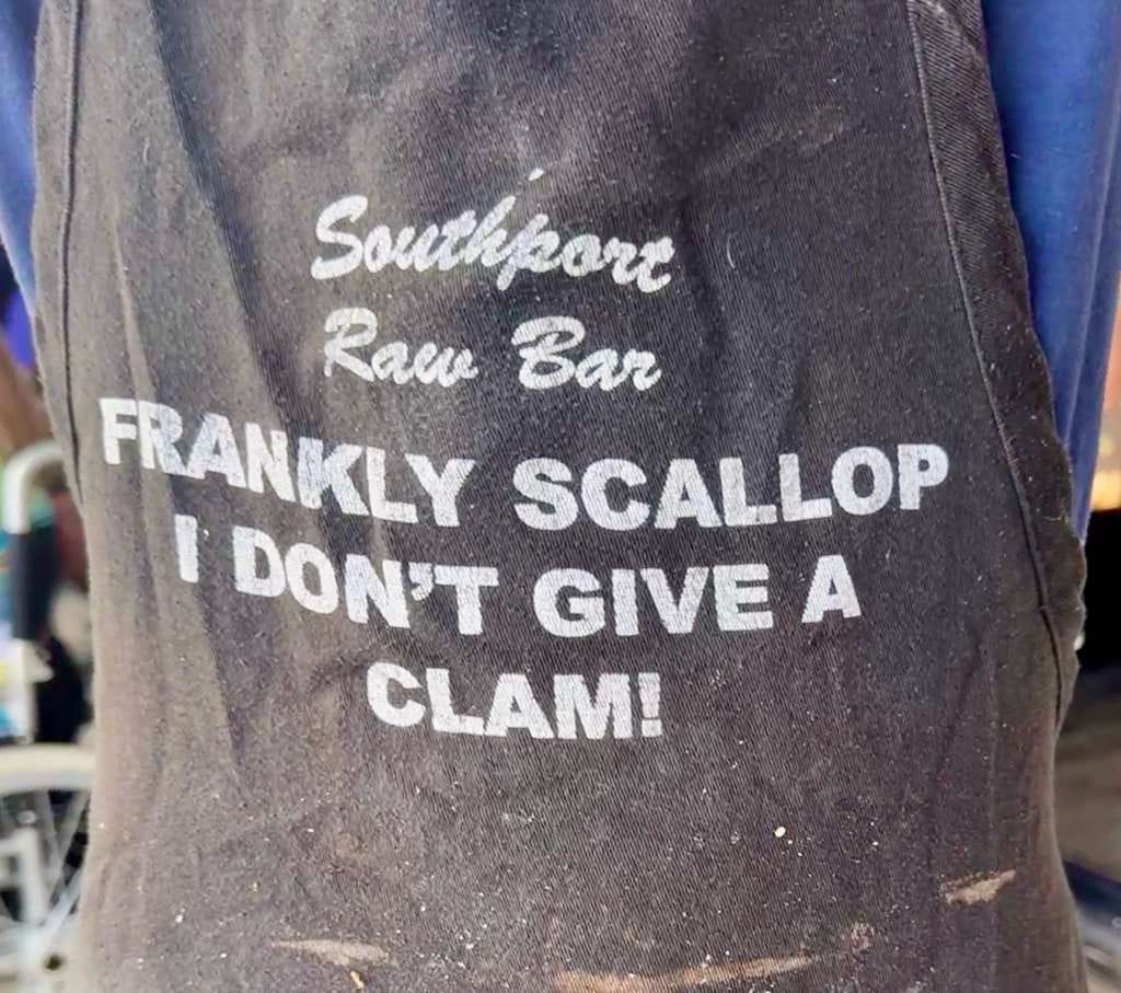 A worn Southport Raw Bar apron that reads “Frankly Scallop, I don’t give a clam!”
