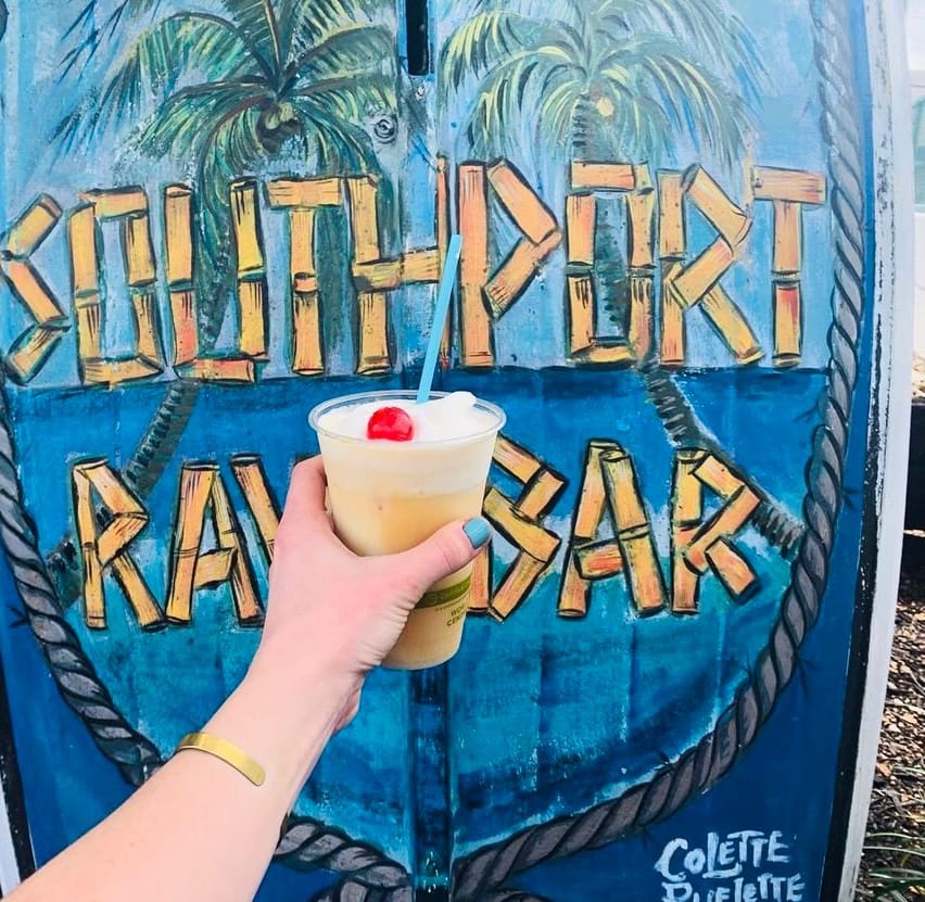 Southport Raw Bar hand-painted on an old boat, a frozen drink with a cherry held up in front