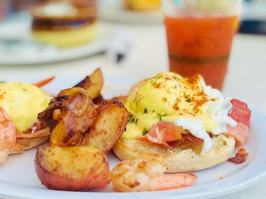 Eggs Benedict with shrimp and bacon, roasted potatoes beside them and a Bloody Mary behind