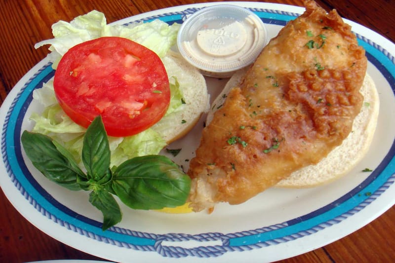 Fried fish fillet sandwich with lettuce, tomato and a side of sauce