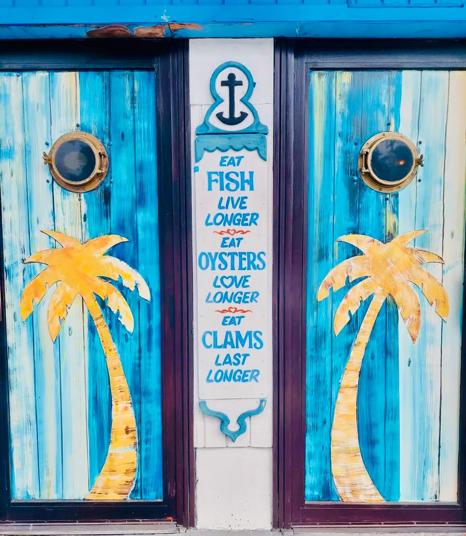 The blue doors with porthole windows, palm trees and the Eat Fish, Eat Oysters, Eat Clams sign