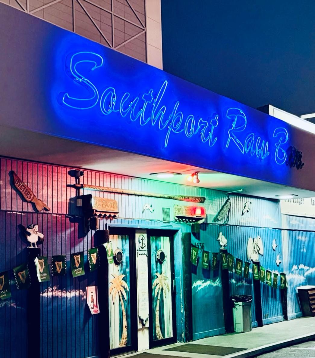 The Southport Raw Bar neon sign glowing blue over the entrance at night