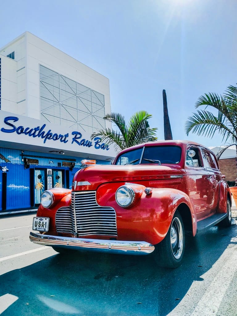 A vintage red car parked by the Southport Raw Bar sign