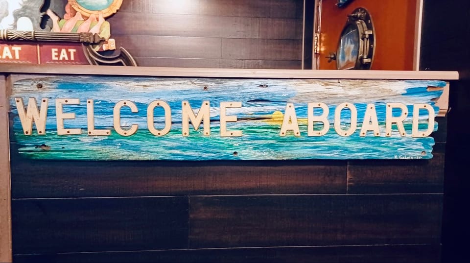A hand-painted Welcome Aboard sign on weathered wood, signed K. Galvin ’86